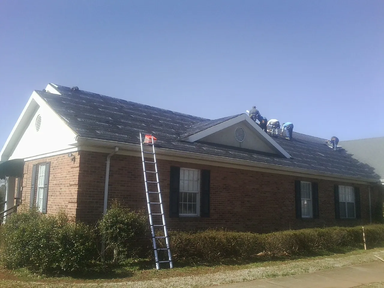 Crew tearing shingles off a brick ranch roof with a ladder set — Metal Roof Repair work by our crew in Margaret
