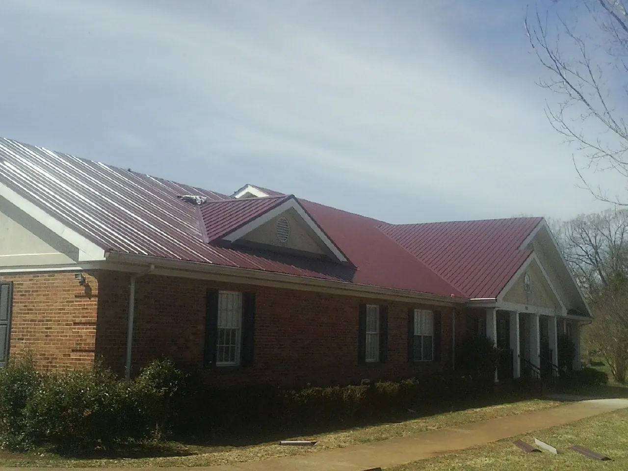 Red metal roof with gabled entries on a long brick building, from a Hail Damage Roof Repair job in Margaret