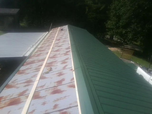Old rusted panels beside newly installed green metal roofing — Wind Damage Roof Repair by Roofing Brothers in Margaret