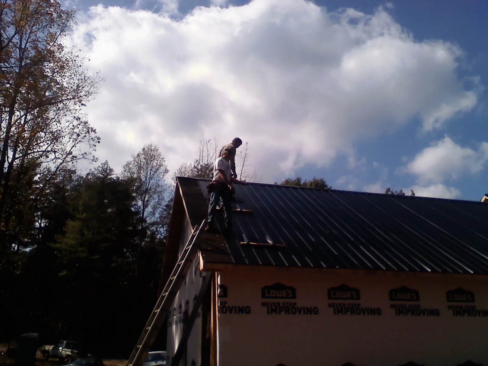 Roofer fastening dark metal panels high against a cloudy sky, from a Roof Inspection job in Margaret