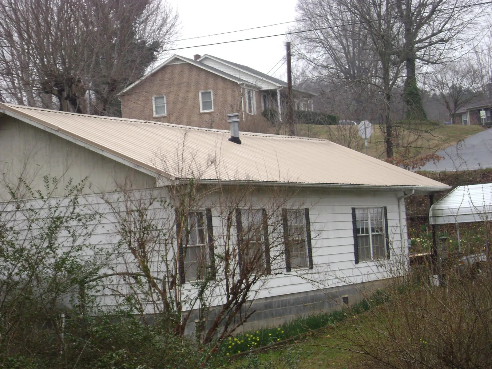 Tan metal roof on a white sided house set into a hillside — Commercial Roofing by Roofing Brothers in Margaret