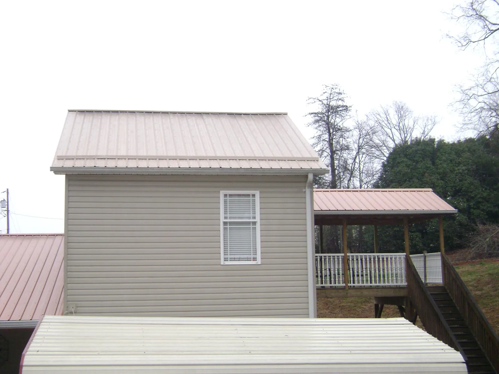 Tan metal roofs on a two story addition and attached porch, from a Roof Replacement job in Margaret